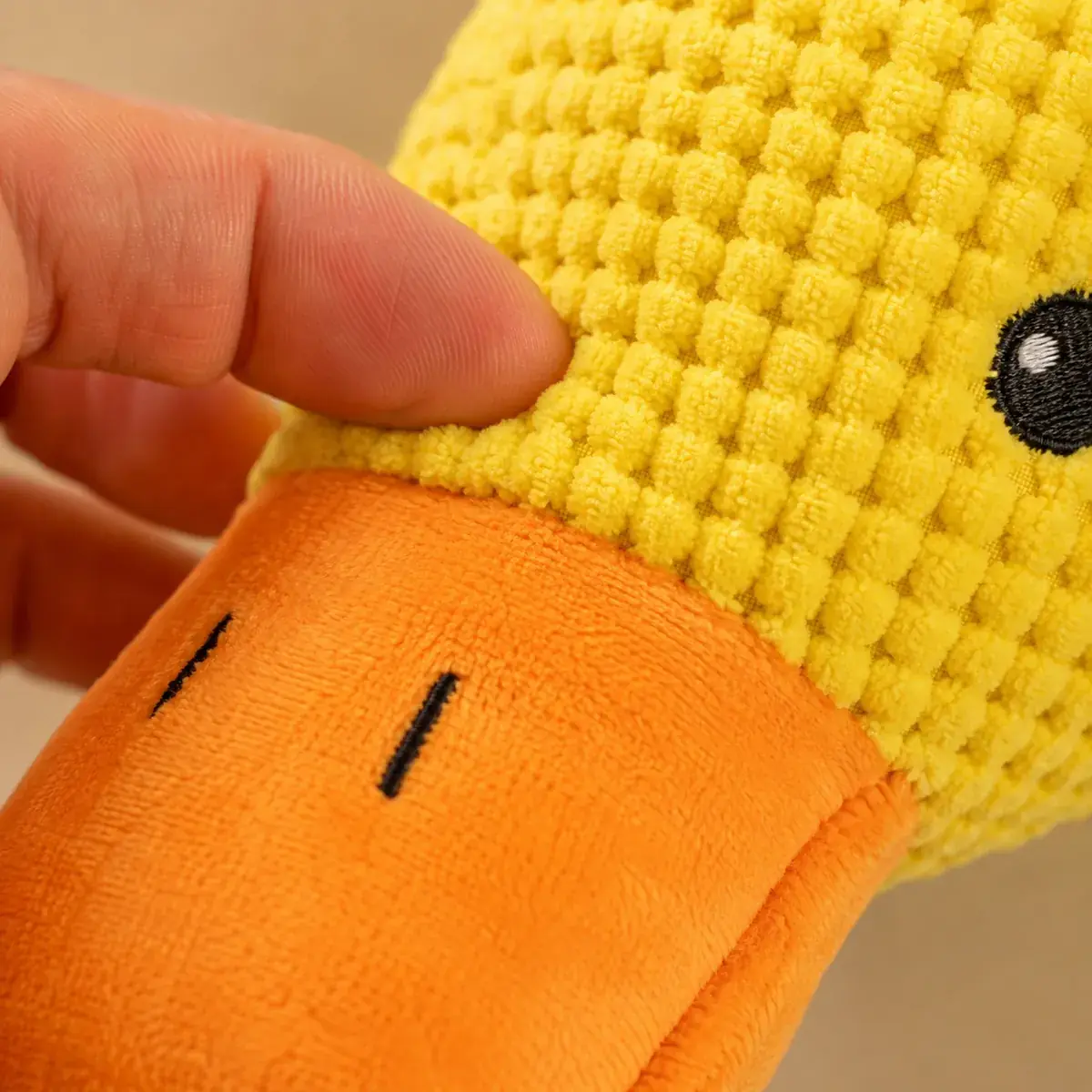 Gros plan sur le tissu gaufré jaune et le bec orange du canard, pincé entre deux doigts